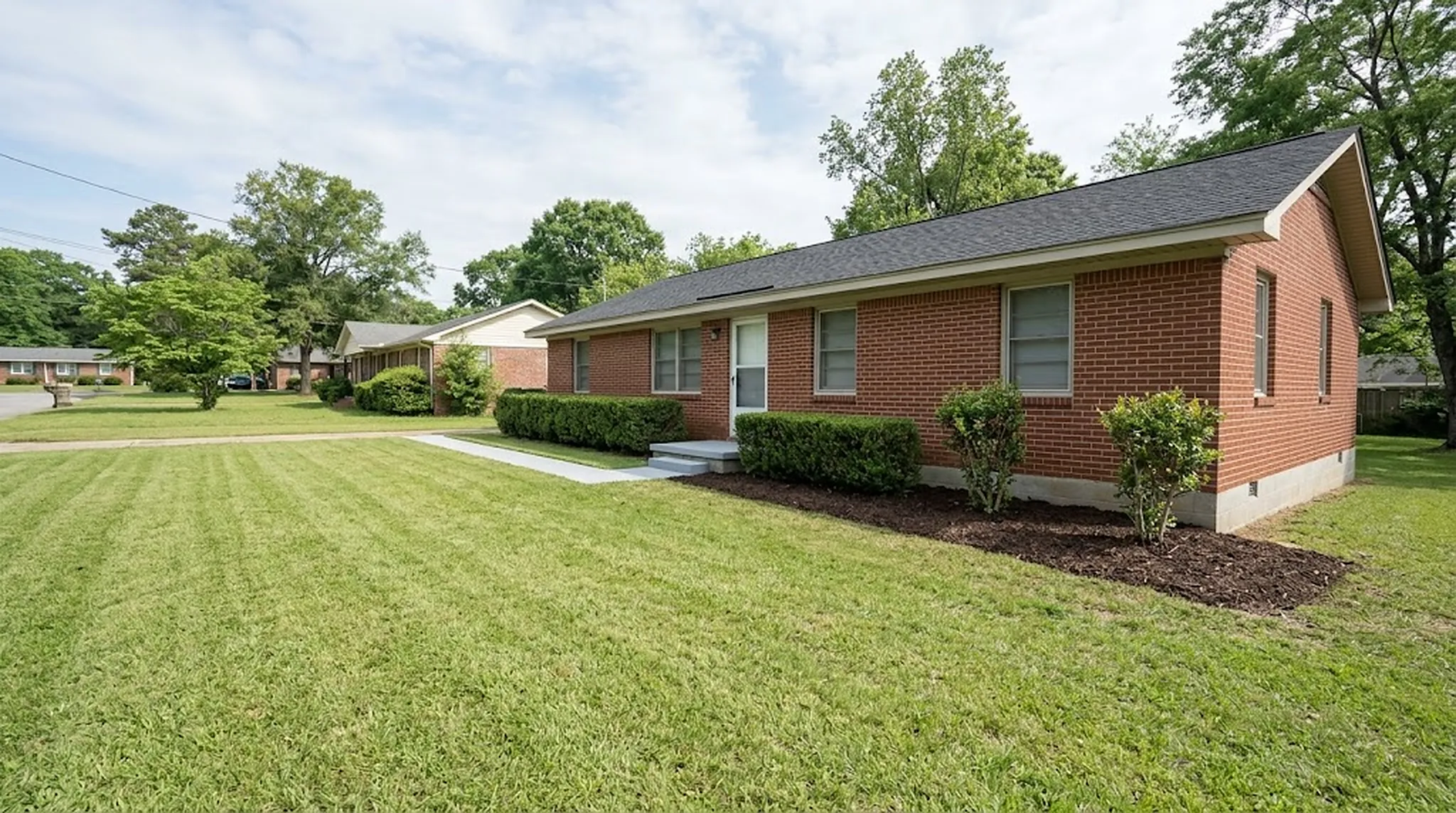 Freshly mown striped lawn beside a brick house with trimmed shrubs and fresh mulch